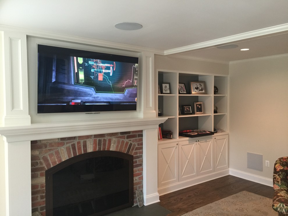 This is an example of a mid-sized traditional enclosed family room in DC Metro with beige walls, medium hardwood floors, a standard fireplace, a brick fireplace surround, a wall-mounted tv and brown floor.