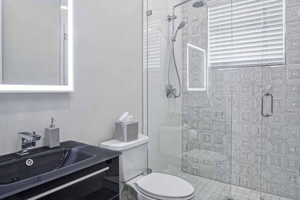 Inspiration for a mid-sized modern 3/4 bathroom in Miami with flat-panel cabinets, black cabinets, an open shower, a one-piece toilet, gray tile, porcelain tile, white walls, an integrated sink, engineered quartz benchtops, a hinged shower door, black benchtops, a single vanity and a built-in vanity.