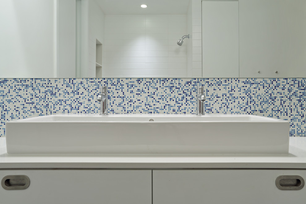 Large modern master bathroom in New York with flat-panel cabinets, white cabinets, a freestanding tub, an alcove shower, blue tile, white tile, mosaic tile, white walls, solid surface benchtops, porcelain floors and a drop-in sink.