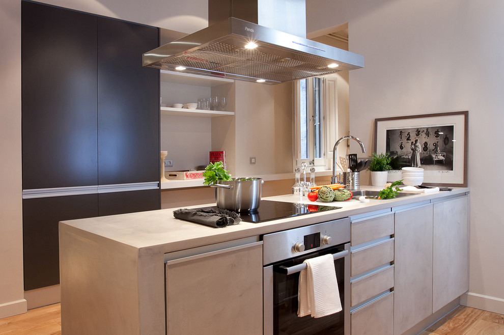 Inspiration for a small transitional galley separate kitchen in Barcelona with a drop-in sink, flat-panel cabinets, grey cabinets, solid surface benchtops, stainless steel appliances, light hardwood floors and with island.