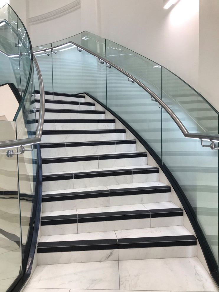 Diseño de escalera curva moderna extra grande con escalones con baldosas, contrahuellas con baldosas y/o azulejos, barandilla de vidrio y todos los tratamientos de pared