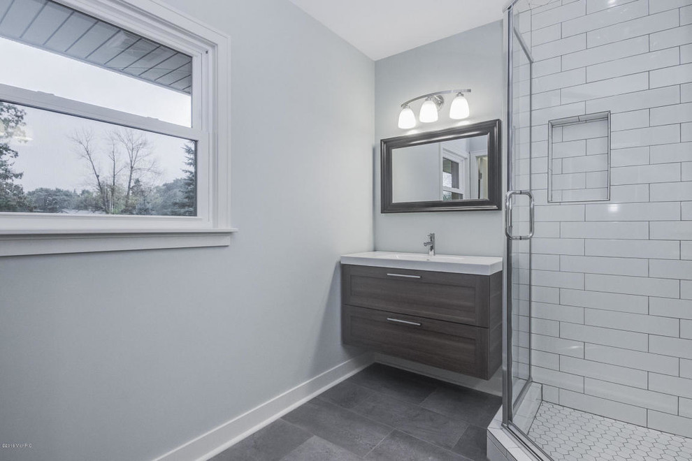 This is an example of a mid-sized transitional master bathroom in Grand Rapids with a corner shower, grey walls, an integrated sink, shaker cabinets, dark wood cabinets, white tile, ceramic tile, vinyl floors and solid surface benchtops.
