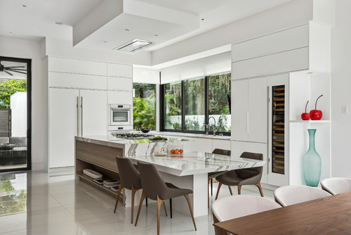 Bright modern kitchen with white handleless cabinets, marble waterfall island, and large windows