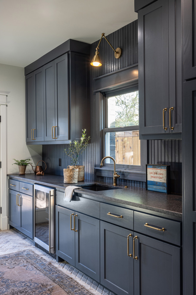 ダラスにある高級な中くらいなトランジショナルスタイルのおしゃれな家事室 (ll型、アンダーカウンターシンク、シェーカースタイル扉のキャビネット、青いキャビネット、御影石カウンター、青いキッチンパネル、塗装板のキッチンパネル、青い壁、レンガの床、左右配置の洗濯機・乾燥機、茶色い床、黒いキッチンカウンター、塗装板張りの壁) の写真