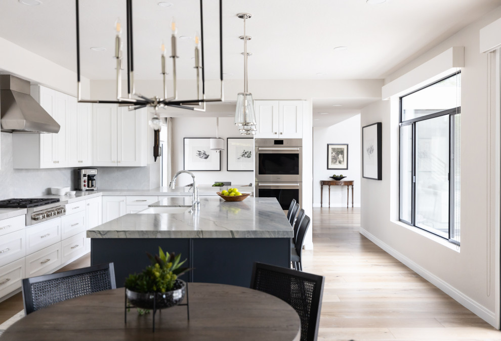 Inspiration for a large transitional medium tone wood floor and brown floor eat-in kitchen remodel in Phoenix with a farmhouse sink, recessed-panel cabinets, white cabinets, quartzite countertops, beige backsplash, stone slab backsplash, paneled appliances, an island and gray countertops