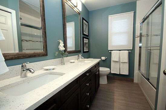 Mid-sized transitional 3/4 dark wood floor and brown floor alcove shower photo with recessed-panel cabinets, black cabinets, a two-piece toilet, blue walls, an undermount sink, quartz countertops and gray countertops