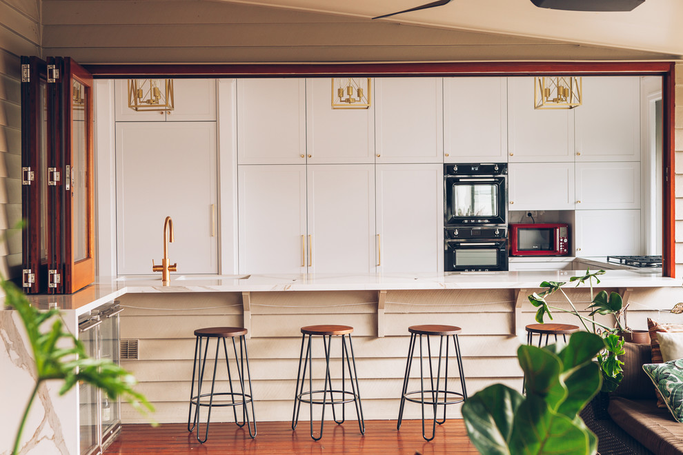 Design ideas for a traditional kitchen in Brisbane with an undermount sink, shaker cabinets, white cabinets, granite benchtops, black appliances, light hardwood floors, brown floor and white benchtop.