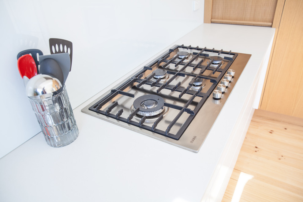 This is an example of a mid-sized scandinavian u-shaped eat-in kitchen in Melbourne with an undermount sink, flat-panel cabinets, white cabinets, granite benchtops, white splashback, glass sheet splashback, a peninsula, stainless steel appliances, light hardwood floors and grey benchtop.