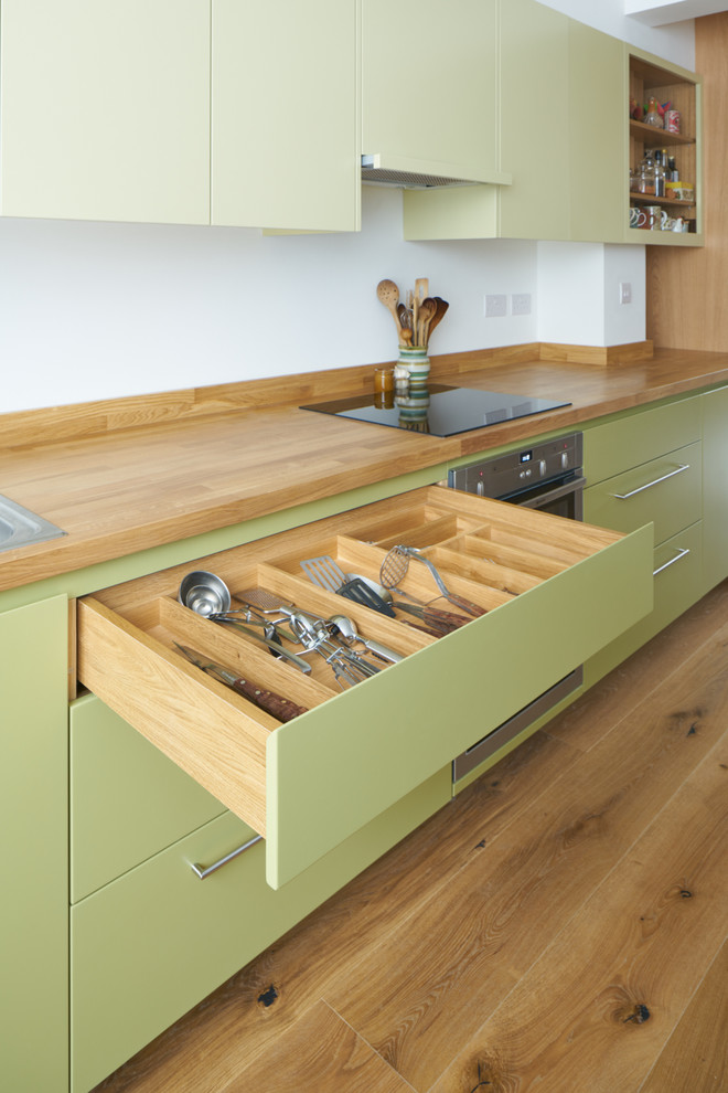 Design ideas for a mid-sized contemporary single-wall open plan kitchen in London with a double-bowl sink, flat-panel cabinets, green cabinets, wood benchtops, panelled appliances, light hardwood floors and no island.