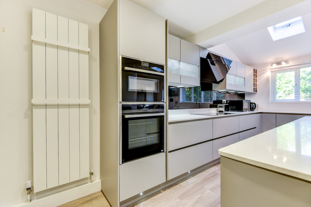 Foto på ett stort funkis vit kök, med en undermonterad diskho, släta luckor, grå skåp, bänkskiva i kvartsit, svart stänkskydd, glaspanel som stänkskydd, svarta vitvaror, vinylgolv, en köksö och grått golv