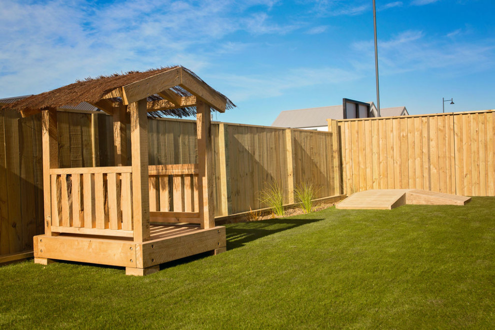 Mid-sized country front yard partial sun garden in Christchurch with with outdoor playset and decking.