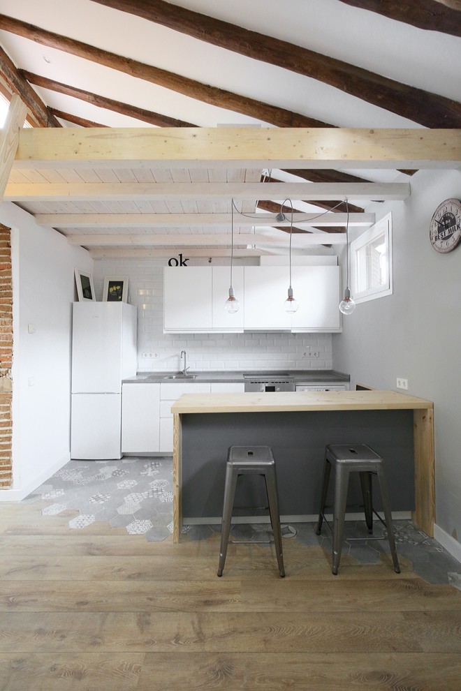 Photo of a mid-sized scandinavian galley open plan kitchen in Madrid with flat-panel cabinets, white cabinets, white splashback, subway tile splashback, a peninsula and white appliances.