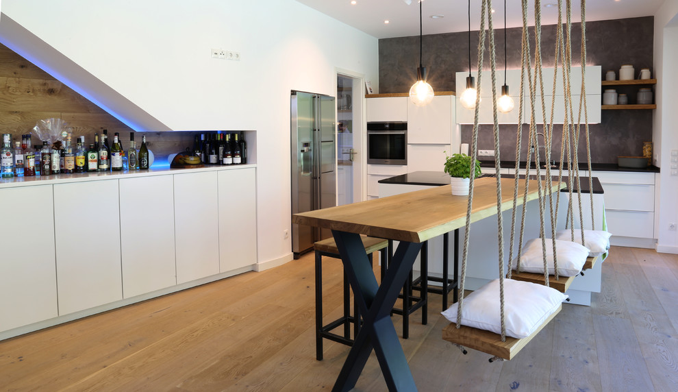 This is an example of a large contemporary l-shaped open plan kitchen in Bremen with flat-panel cabinets, white cabinets, wood benchtops, grey splashback, stainless steel appliances, medium hardwood floors, with island, brown floor and beige benchtop.