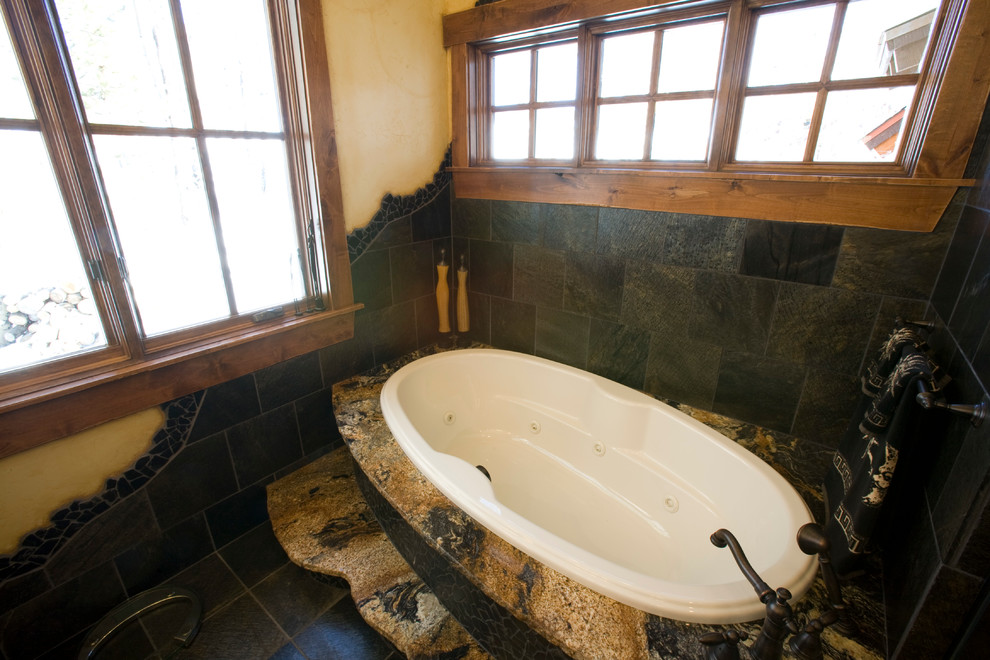 This is an example of a mid-sized country master bathroom in Denver with raised-panel cabinets, black cabinets, a drop-in tub, a two-piece toilet, black tile, stone tile, yellow walls, granite benchtops, a corner shower and slate floors.