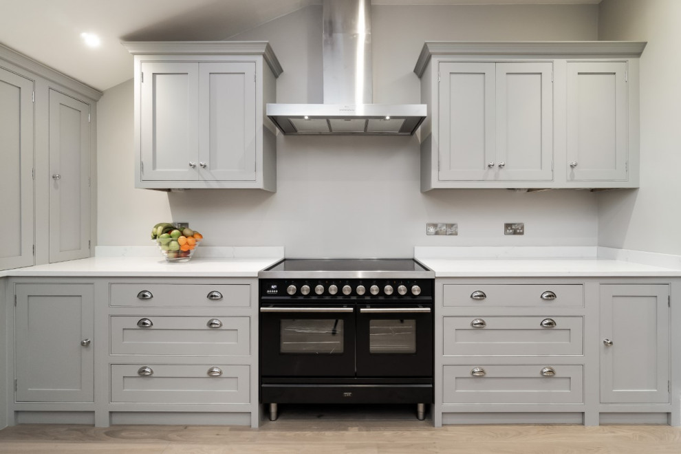 Mittelgroße Klassische Küche in U-Form mit Kassettenfronten, grauen Schränken, schwarzen Elektrogeräten, Halbinsel und weißer Arbeitsplatte in Surrey