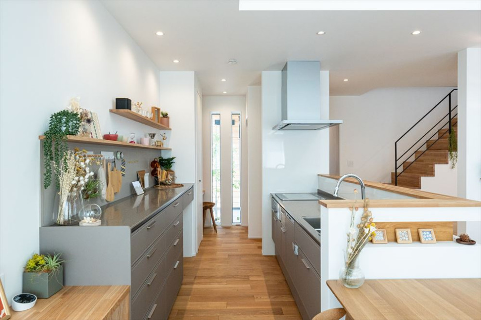 Photo of a contemporary single-wall open plan kitchen in Other with an undermount sink, beaded inset cabinets, solid surface benchtops, brown splashback, shiplap splashback, stainless steel appliances, medium hardwood floors, with island, brown floor, grey benchtop and wallpaper.