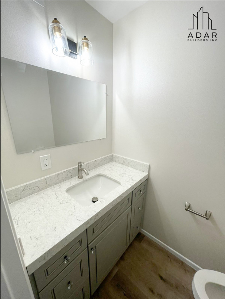 Exemple d'un petit WC et toilettes moderne avec un placard à porte affleurante, des portes de placard grises, un mur blanc, parquet clair, un plan de toilette en marbre, un sol marron, un plan de toilette blanc et meuble-lavabo encastré.