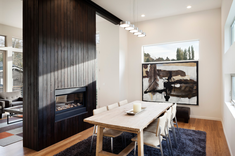 Photo of a modern open plan dining in Seattle with bamboo floors, a two-sided fireplace and a wood fireplace surround.