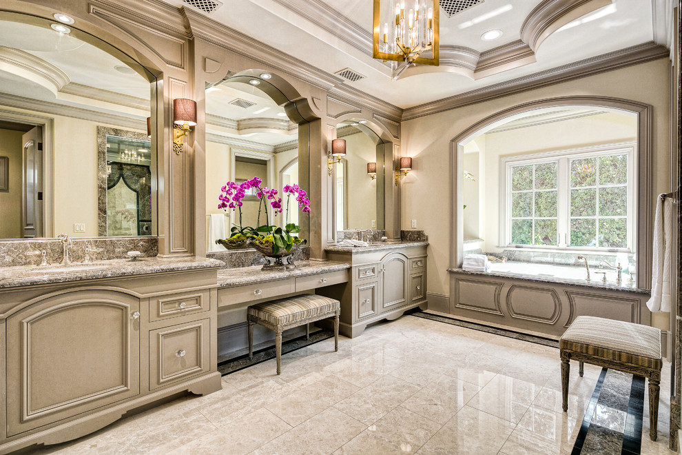 This is an example of a transitional master bathroom in Los Angeles with recessed-panel cabinets, grey cabinets, an undermount tub, an alcove shower, beige walls, marble floors, an undermount sink, granite benchtops, white floor, a hinged shower door and multi-coloured benchtops.