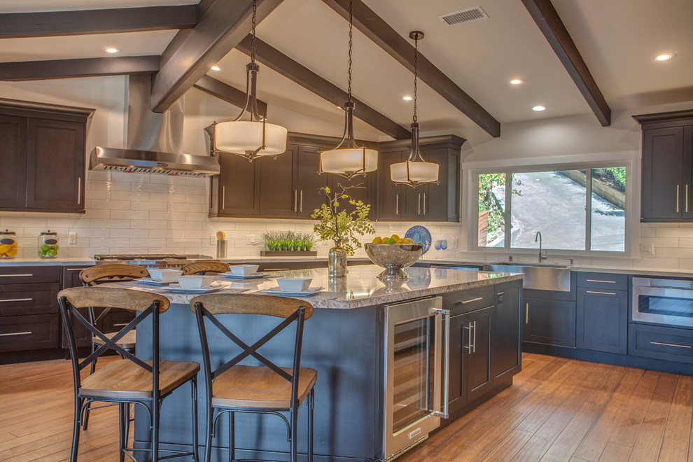 Inspiration for an expansive arts and crafts l-shaped eat-in kitchen in San Francisco with a farmhouse sink, shaker cabinets, dark wood cabinets, quartzite benchtops, white splashback, ceramic splashback, stainless steel appliances, medium hardwood floors, with island and brown floor.
