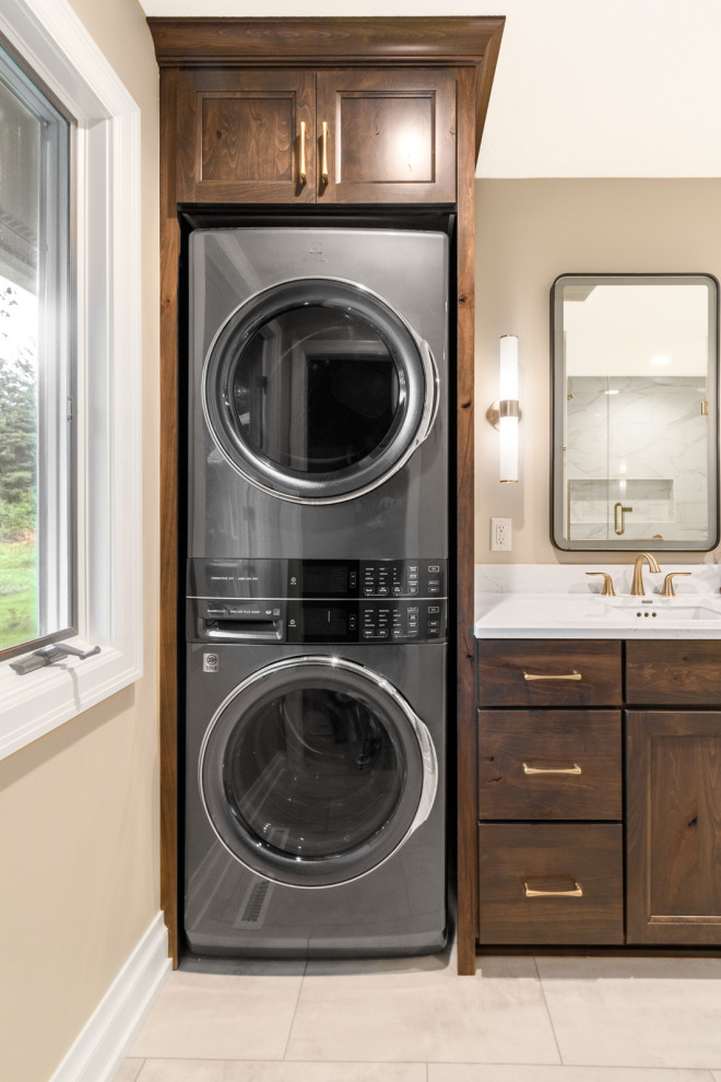 Inspiration for a transitional galley porcelain tile and beige floor laundry room remodel in Minneapolis with an undermount sink, recessed-panel cabinets, dark wood cabinets, quartz countertops, beige walls, a stacked washer/dryer and white countertops