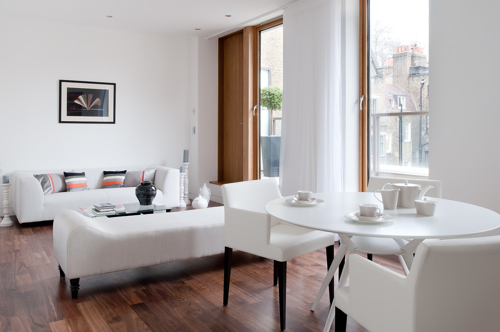 This is an example of a contemporary open concept living room in London with white walls and dark hardwood floors.