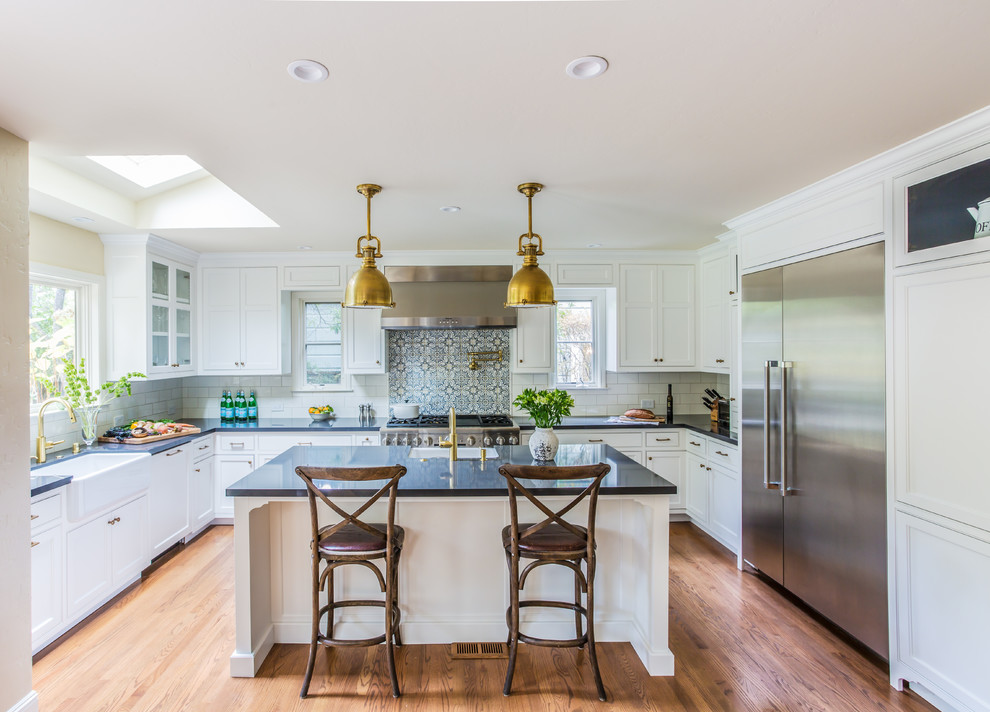 This is an example of a traditional u-shaped kitchen in San Francisco with a farmhouse sink, recessed-panel cabinets, white cabinets, white splashback, subway tile splashback, stainless steel appliances, dark hardwood floors and with island.