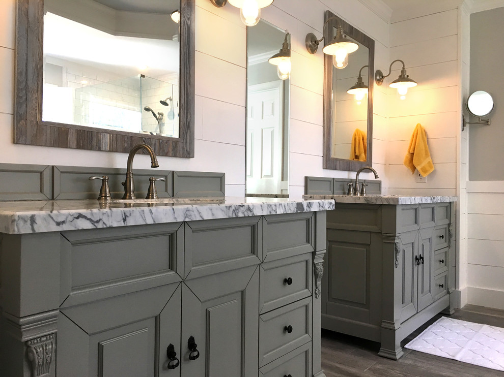 This is an example of a large transitional master bathroom in Atlanta with furniture-like cabinets, grey cabinets, a freestanding tub, a corner shower, a two-piece toilet, white tile, ceramic tile, grey walls, porcelain floors, an undermount sink, marble benchtops, grey floor and a hinged shower door.