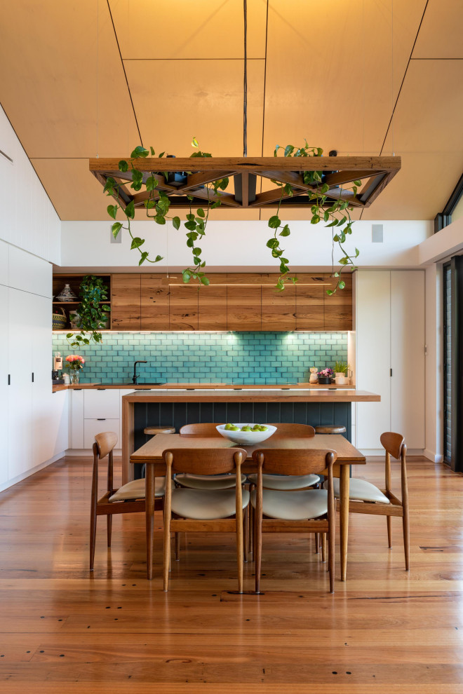 Large contemporary l-shaped eat-in kitchen in Melbourne with a drop-in sink, flat-panel cabinets, white cabinets, wood benchtops, green splashback, subway tile splashback, panelled appliances, medium hardwood floors, with island, brown floor and brown benchtop.