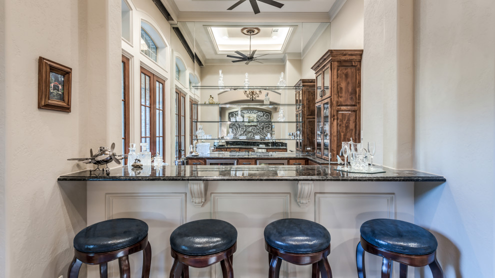 Design ideas for a traditional seated home bar in Houston with glass-front cabinets, dark wood cabinets, mirror splashback and black benchtop.