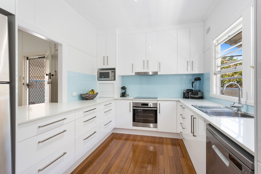 Beach style kitchen in Gold Coast - Tweed with a drop-in sink, white cabinets, quartz benchtops, blue splashback, glass sheet splashback and stainless steel appliances.