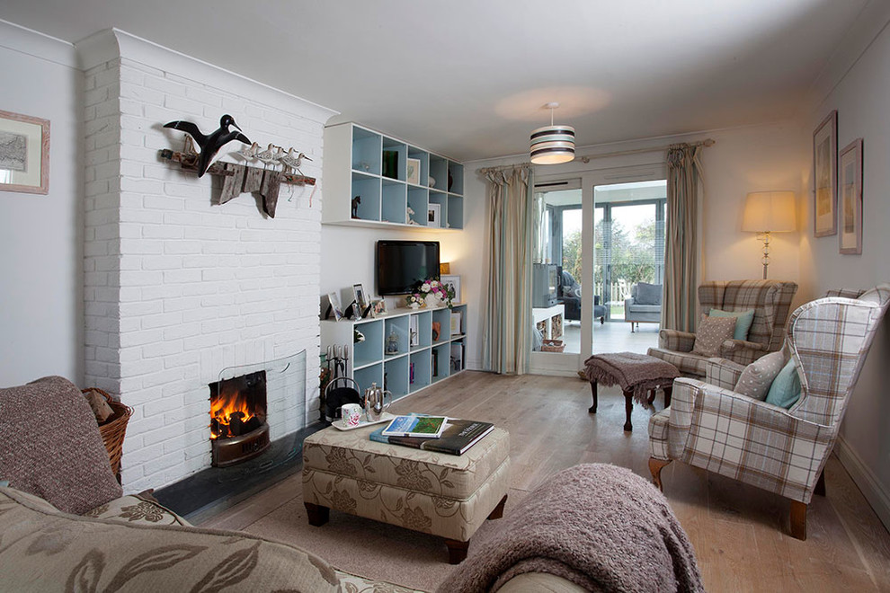 This is an example of a small beach style open concept living room in Cornwall with white walls, medium hardwood floors, a standard fireplace, a brick fireplace surround and a wall-mounted tv.