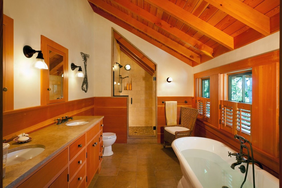 This is an example of a mid-sized country master bathroom in Boston with flat-panel cabinets, medium wood cabinets, a claw-foot tub, an alcove shower, a two-piece toilet, beige tile, stone tile, beige walls, travertine floors, an undermount sink and engineered quartz benchtops.