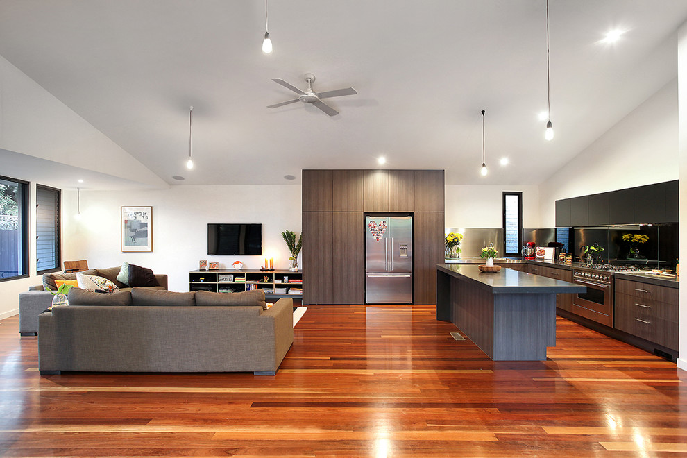 This is an example of a contemporary l-shaped open plan kitchen in Melbourne with flat-panel cabinets, dark wood cabinets, metallic splashback, metal splashback, stainless steel appliances, medium hardwood floors, with island and orange floor.