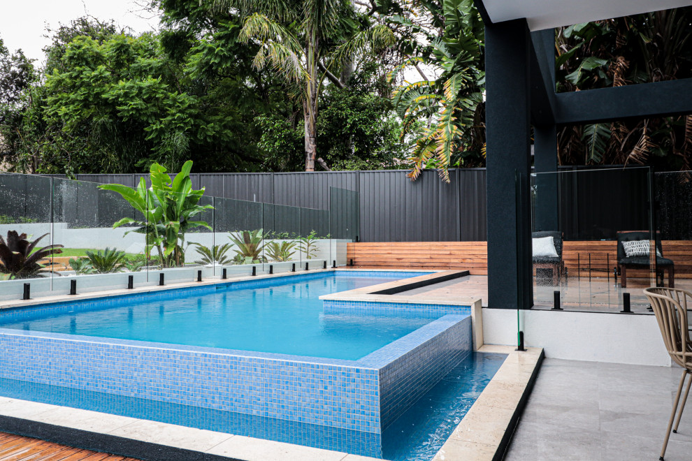 Идея дизайна: наземный, угловой бассейн среднего размера на заднем дворе в стиле модернизм с покрытием из плитки