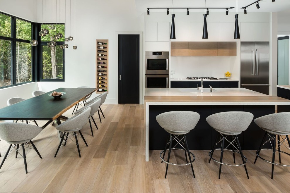 This is an example of a contemporary eat-in kitchen in Toronto with an undermount sink, flat-panel cabinets, white cabinets, white splashback, stainless steel appliances, light hardwood floors, with island and beige floor.