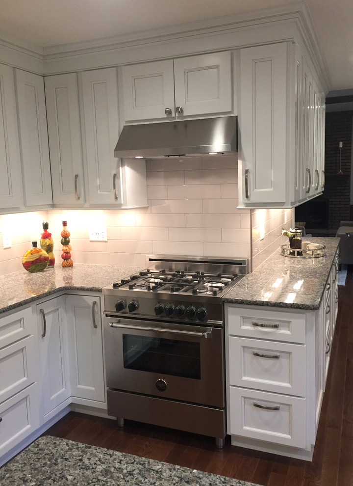 Example of a transitional galley dark wood floor kitchen design with an undermount sink, flat-panel cabinets, white cabinets, granite countertops, white backsplash, porcelain backsplash, stainless steel appliances and an island