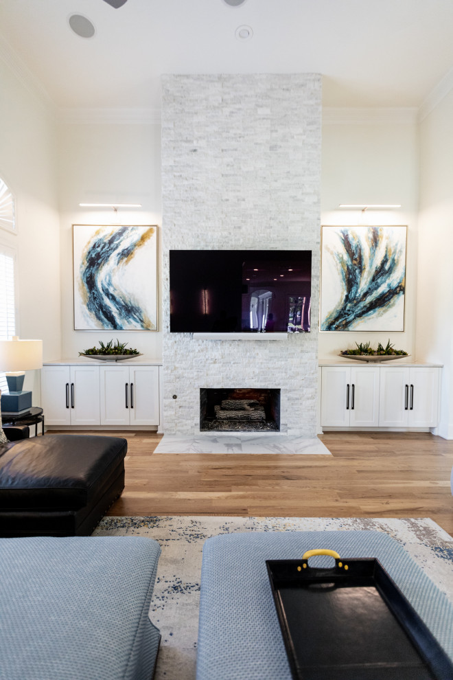 Imagen de sala de estar abierta moderna grande con paredes blancas, suelo de madera clara, todas las chimeneas, piedra de revestimiento, televisor colgado en la pared y suelo marrón