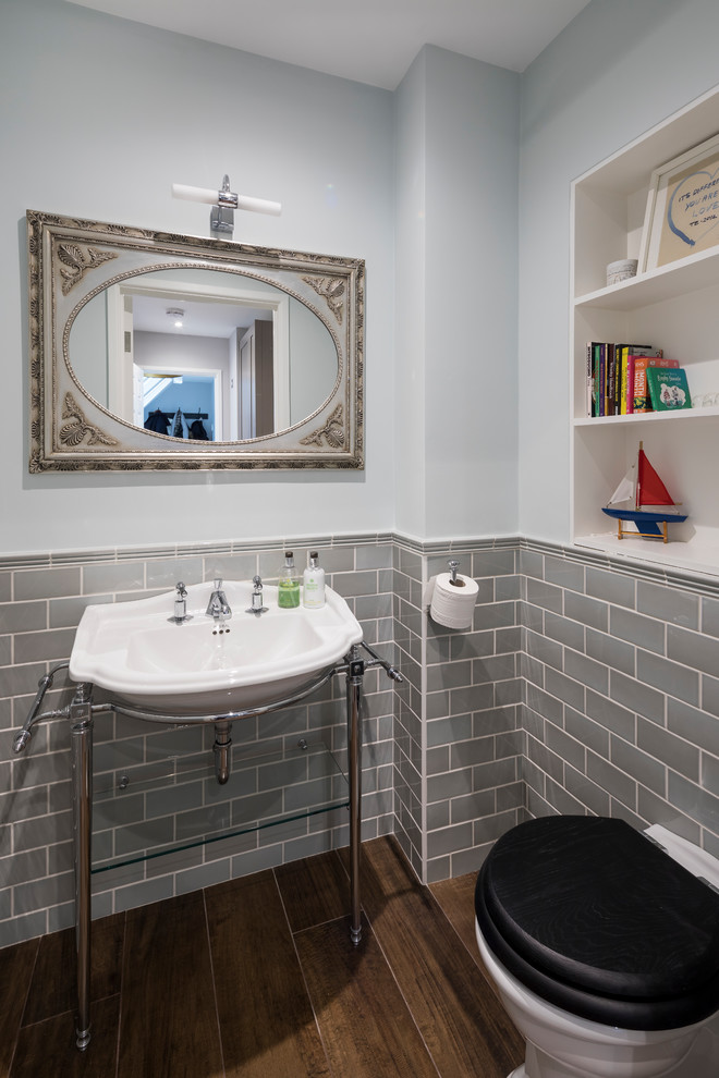 Small traditional kids bathroom in London with a one-piece toilet, gray tile, grey walls, medium hardwood floors, brown floor, subway tile and a console sink.