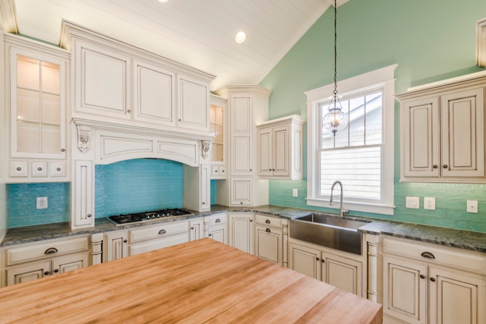 Large transitional u-shaped dark wood floor and brown floor kitchen photo with a farmhouse sink, raised-panel cabinets, beige cabinets, blue backsplash, glass tile backsplash, paneled appliances, an island and gray countertops