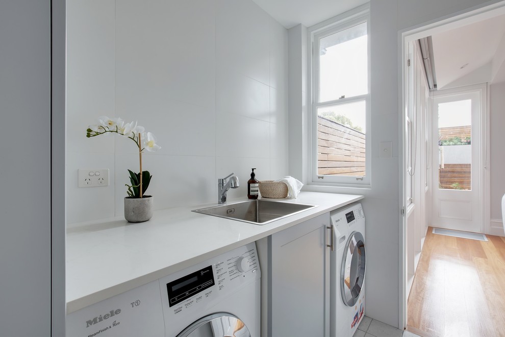 Mid-sized contemporary single-wall dedicated laundry room in Sydney with a single-bowl sink, shaker cabinets, grey cabinets, solid surface benchtops, grey walls, ceramic floors, an integrated washer and dryer, grey floor and white benchtop.