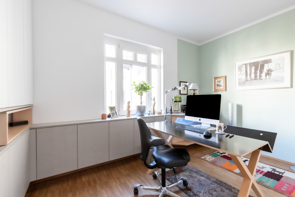 Modelo de despacho contemporáneo pequeño con escritorio independiente, suelo marrón, paredes verdes y suelo de madera en tonos medios