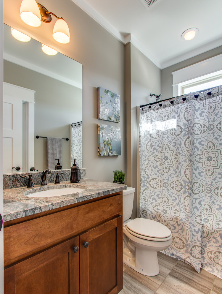 Arts and crafts bathroom in Nashville with flat-panel cabinets, medium wood cabinets, a shower/bathtub combo, a two-piece toilet, ceramic tile, ceramic floors, an undermount sink, granite benchtops and gray tile.