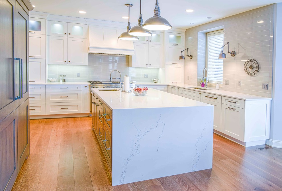 Inspiration for a mid-sized transitional u-shaped medium tone wood floor and brown floor kitchen remodel in Calgary with an undermount sink, flat-panel cabinets, white cabinets, marble countertops, gray backsplash, ceramic backsplash, paneled appliances and an island