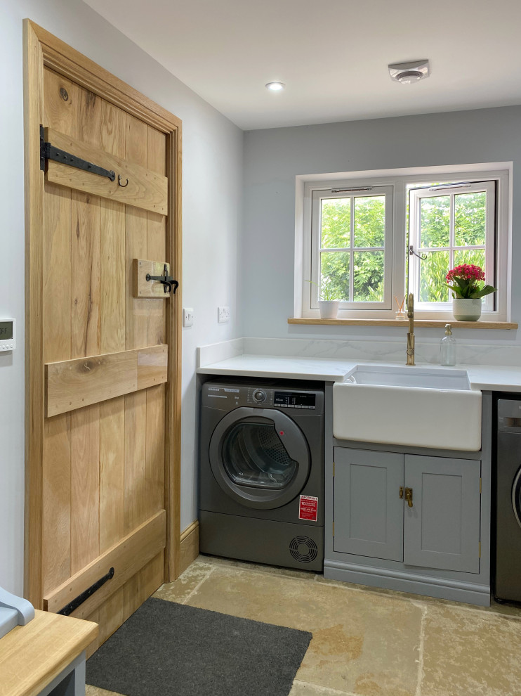 Inspiration for a medium sized contemporary galley separated utility room in Other with a belfast sink, shaker cabinets, blue cabinets, marble worktops, white splashback, marble splashback, white walls, limestone flooring, a side by side washer and dryer, beige floors and white worktops.
