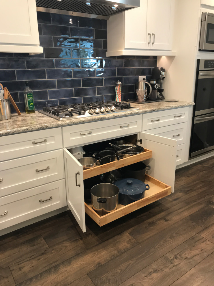 Mid-sized traditional u-shaped kitchen pantry in Dallas with white cabinets, granite benchtops, blue splashback, subway tile splashback, stainless steel appliances, dark hardwood floors, no island, brown floor and brown benchtop.