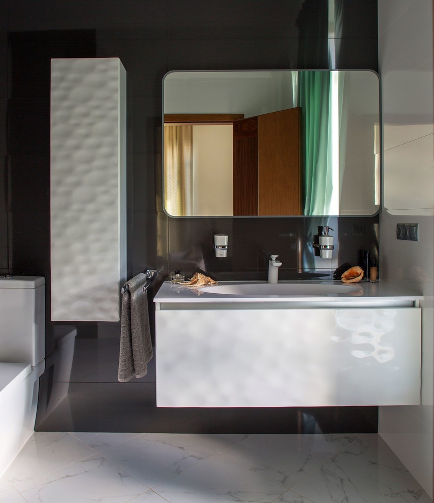 Photo of a large contemporary master bathroom in Moscow with flat-panel cabinets, white cabinets, a two-piece toilet, porcelain tile, marble floors, an integrated sink, solid surface benchtops, white floor, white tile and black tile.