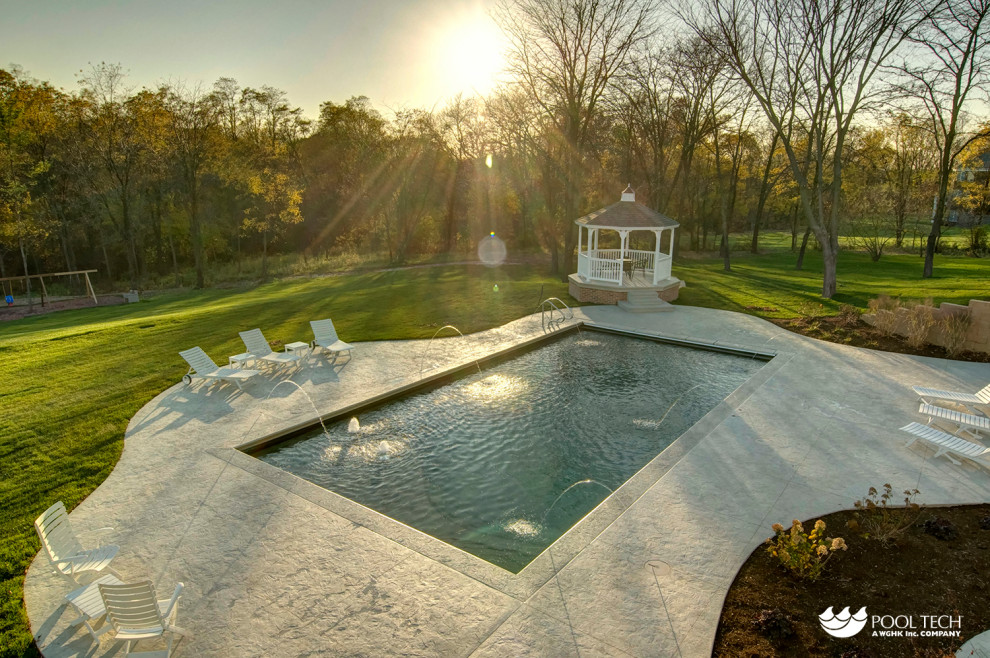 Large mountain style backyard stamped concrete and rectangular pool fountain photo in Cedar Rapids