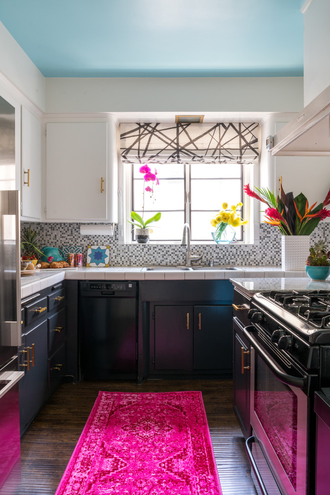 This is an example of a small eclectic u-shaped separate kitchen in Los Angeles with a double-bowl sink, flat-panel cabinets, white cabinets, tile benchtops, multi-coloured splashback, mosaic tile splashback, stainless steel appliances, vinyl floors, no island, brown floor and white benchtop.