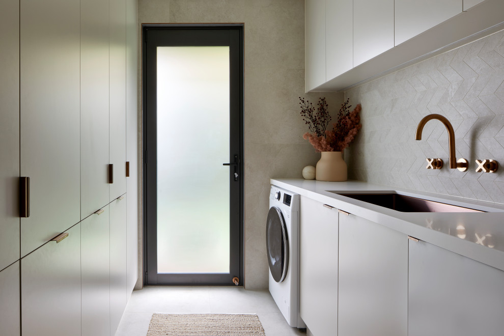 Design ideas for a small contemporary galley dedicated laundry room in Melbourne with an undermount sink, grey cabinets, quartz benchtops, beige splashback, mosaic tile splashback, beige walls, porcelain floors, an integrated washer and dryer, beige floor and white benchtop.